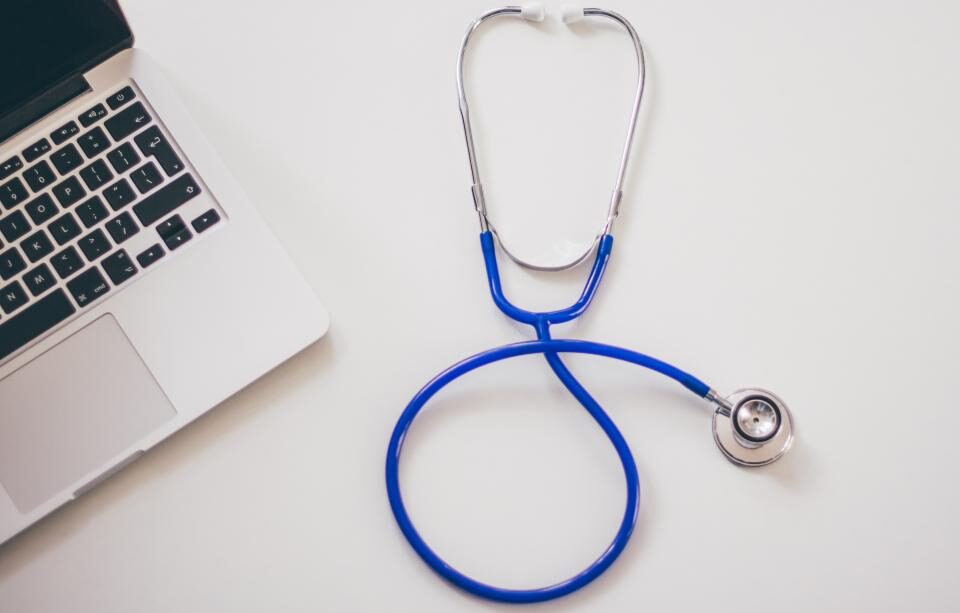 A laptop and a stethoscope on a practice desk
